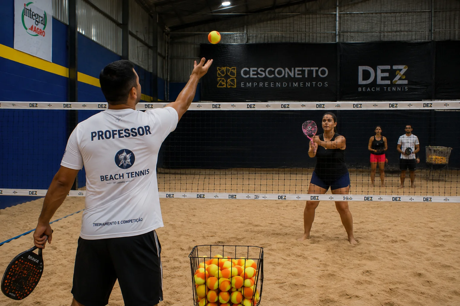 Professor orientando uma aluna durante aula de Beach Tennis em arena coberta