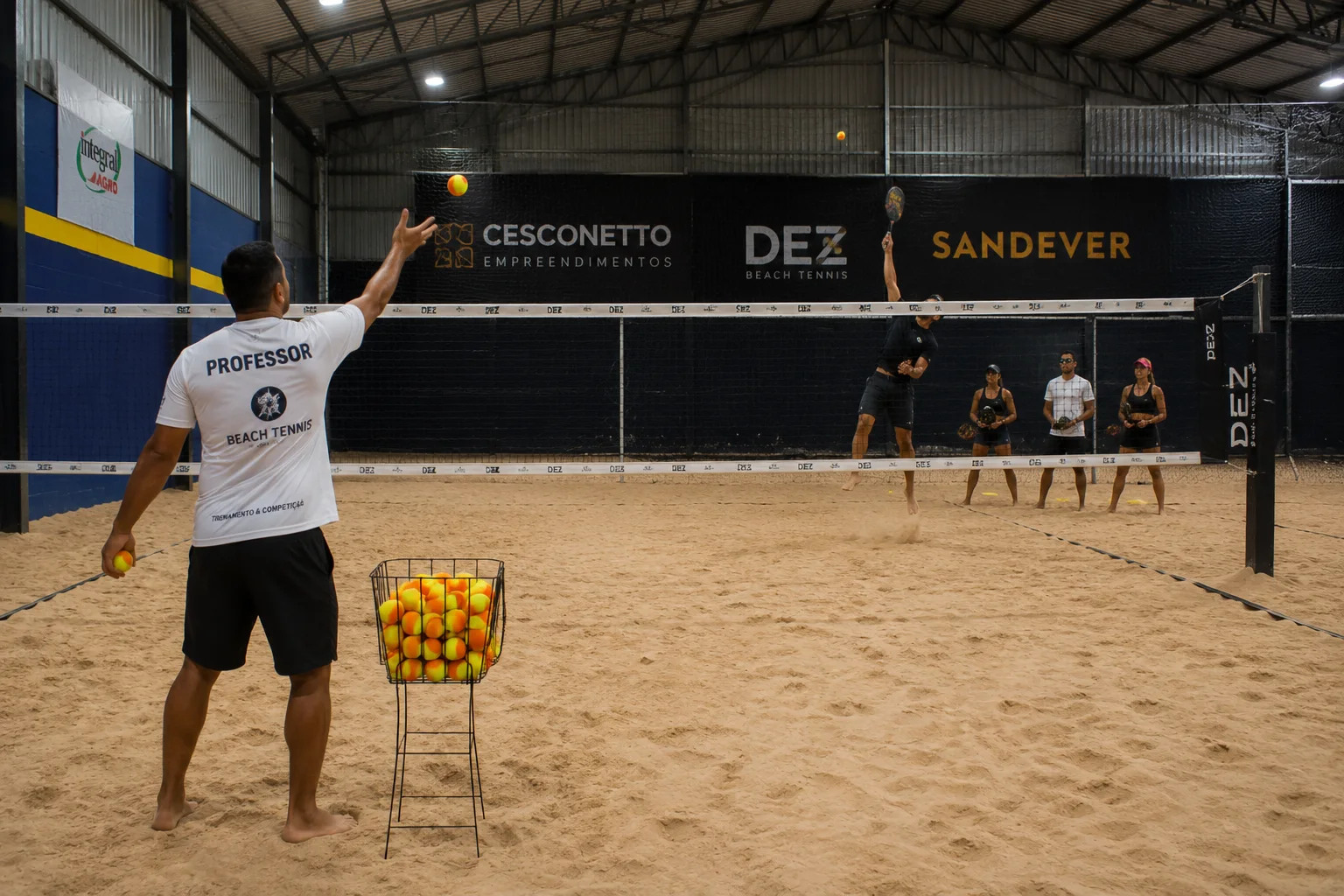 Professor orientando uma turma durante exercício de smash em quadra de Beach Tennis
